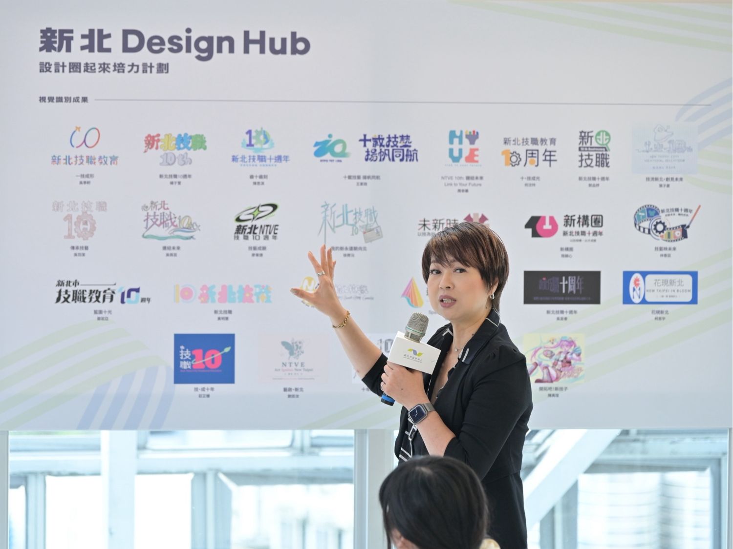 新北市政府副秘書長龔雅雯致詞,身後展示參與學生設計的Logo作品,展現青年創意成果